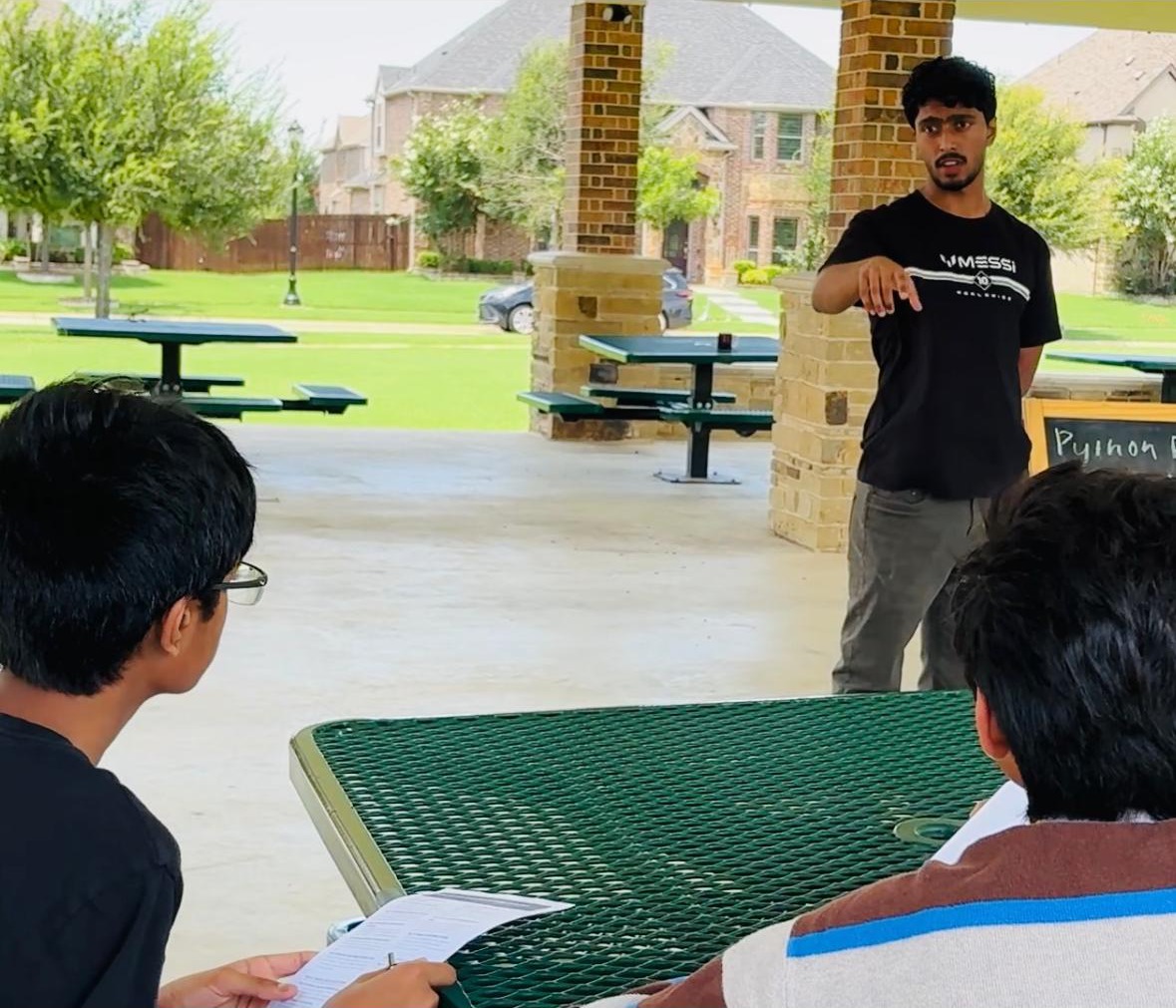Deeptanshu presenting to students seated at an outdoor picnic table during a KidCode session
