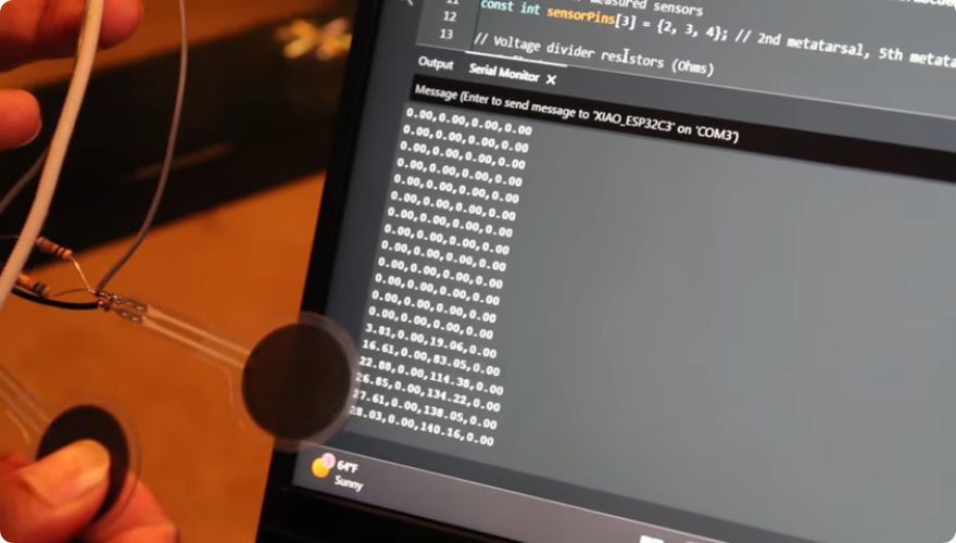 A force sensor held in front of a laptop showing serial output